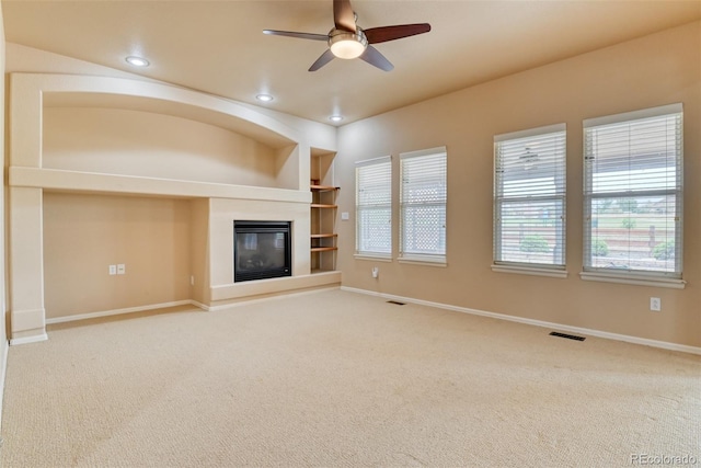 unfurnished living room with built in features, ceiling fan, and carpet flooring