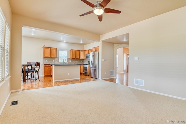 kitchen with sink, stainless steel appliances, a kitchen island, decorative backsplash, and light colored carpet