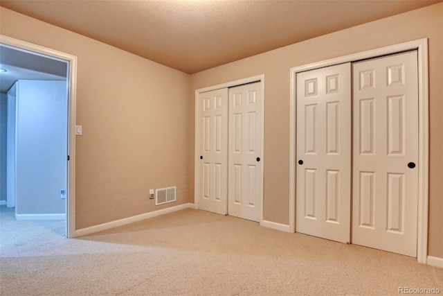 unfurnished bedroom featuring light colored carpet and two closets