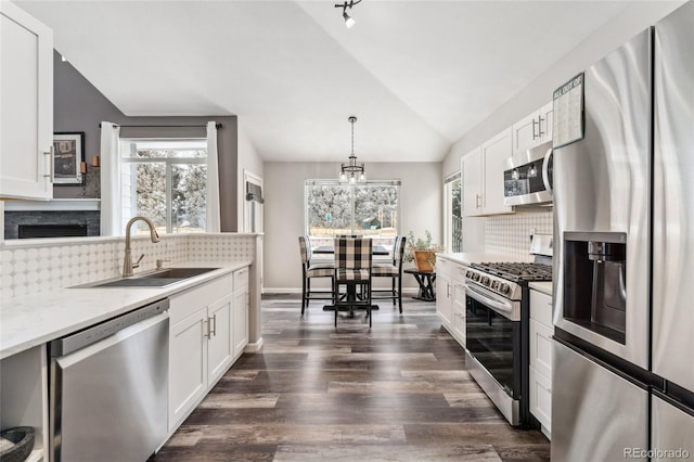 kitchen with lofted ceiling, hanging light fixtures, sink, appliances with stainless steel finishes, and white cabinetry