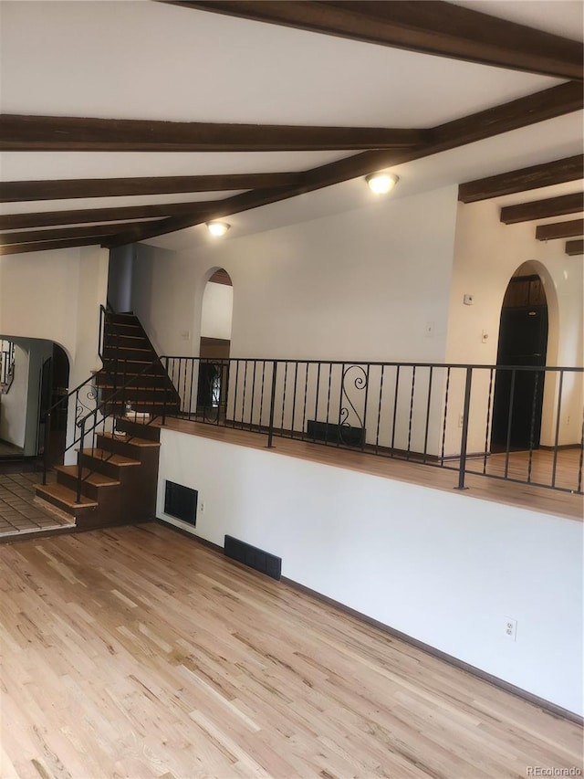 spare room featuring vaulted ceiling with beams and light hardwood / wood-style flooring