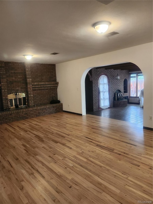 unfurnished living room featuring hardwood / wood-style flooring, brick wall, and a brick fireplace