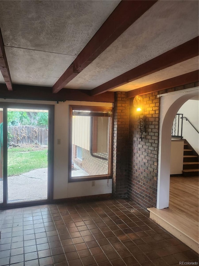 doorway with tile patterned flooring, brick wall, and beam ceiling