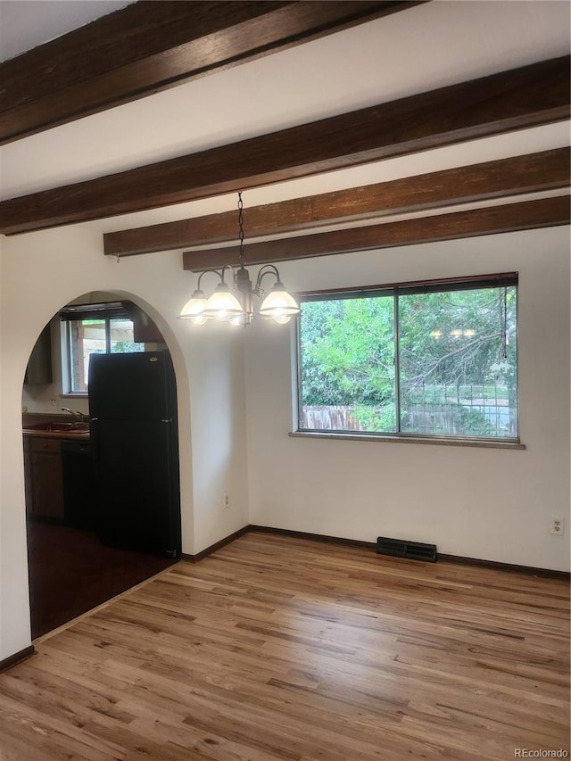 spare room featuring hardwood / wood-style flooring, beam ceiling, plenty of natural light, and an inviting chandelier