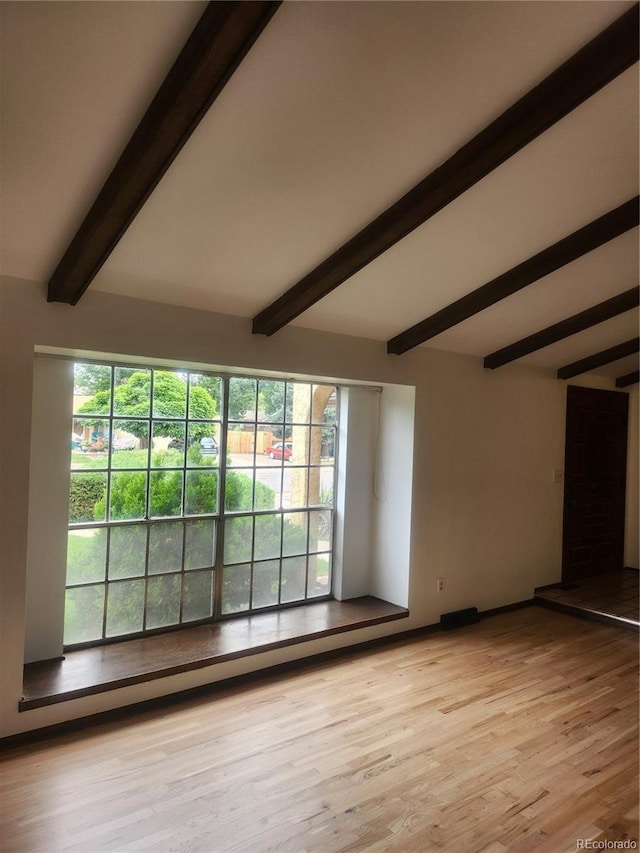 unfurnished room with light wood-type flooring and lofted ceiling with beams