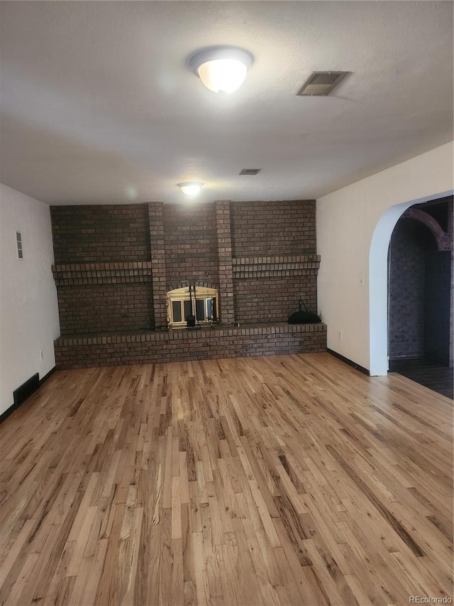 unfurnished living room featuring a fireplace, light hardwood / wood-style flooring, and brick wall