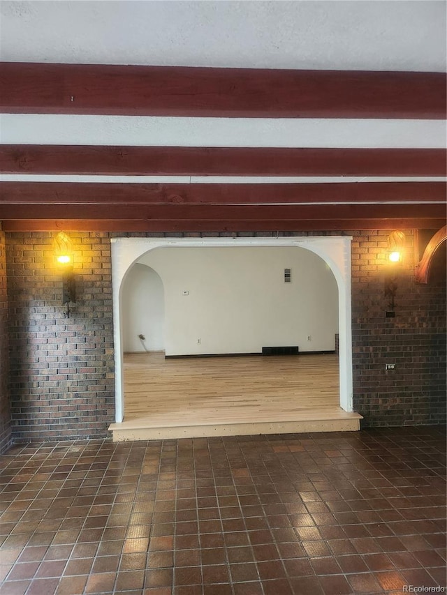 unfurnished room with beamed ceiling, dark tile patterned floors, and brick wall