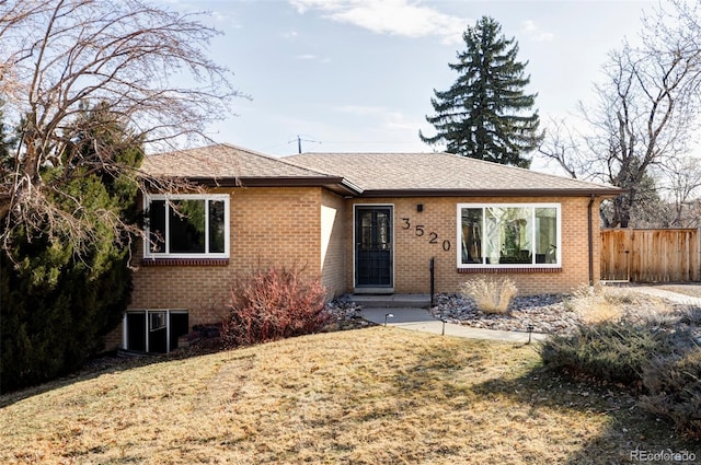 ranch-style home featuring a shingled roof, a front yard, fence, and brick siding