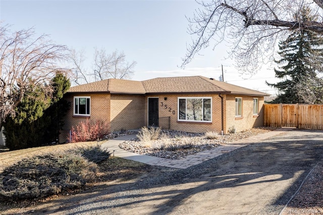 single story home featuring roof with shingles, fence, and brick siding