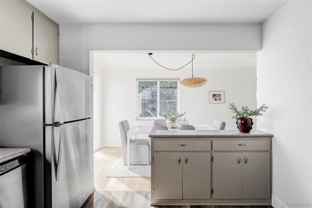 kitchen with light wood finished floors, stainless steel appliances, hanging light fixtures, gray cabinetry, and a peninsula