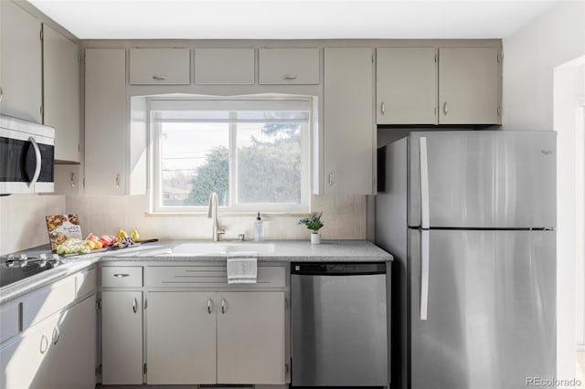 kitchen featuring appliances with stainless steel finishes, gray cabinets, a sink, and backsplash