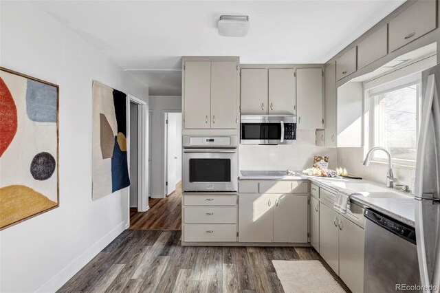 kitchen featuring a sink, light countertops, appliances with stainless steel finishes, gray cabinets, and dark wood-style floors