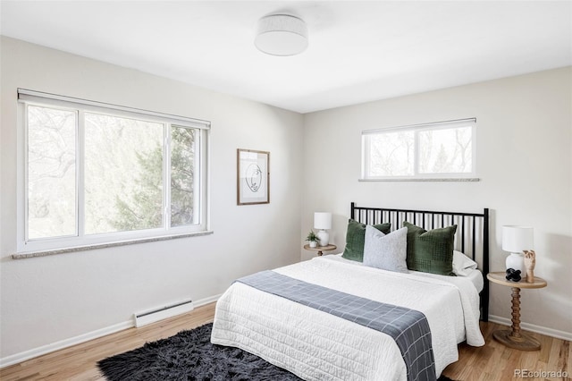 bedroom featuring a baseboard radiator, multiple windows, and wood finished floors