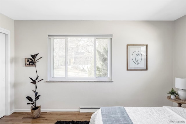 bedroom with a baseboard radiator, baseboards, and wood finished floors