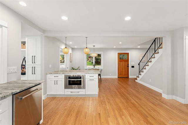 kitchen featuring white cabinetry, hanging light fixtures, stainless steel appliances, light stone counters, and light hardwood / wood-style flooring