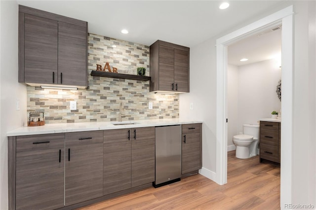 kitchen featuring decorative backsplash, stainless steel fridge, dark brown cabinets, sink, and light hardwood / wood-style floors