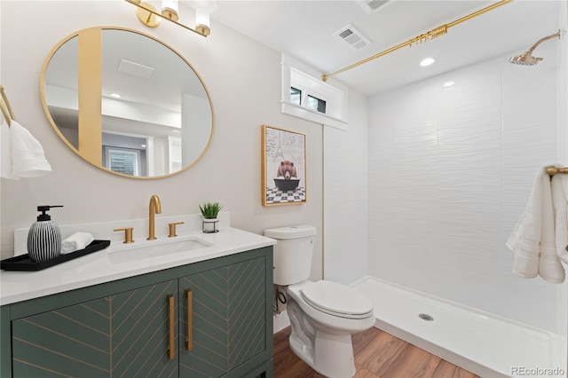 bathroom with hardwood / wood-style flooring, vanity, toilet, and tiled shower