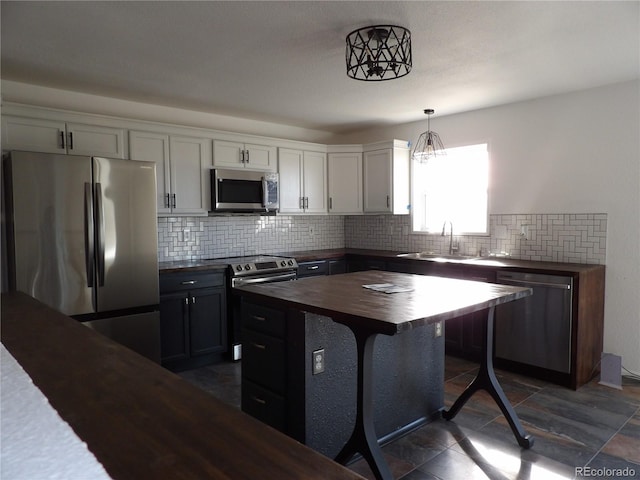 kitchen with stainless steel appliances, sink, white cabinetry, hanging light fixtures, and butcher block counters