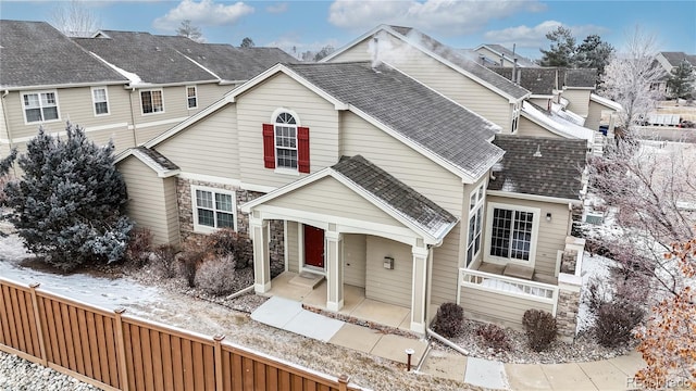 view of front of house featuring a residential view, stone siding, roof with shingles, and fence