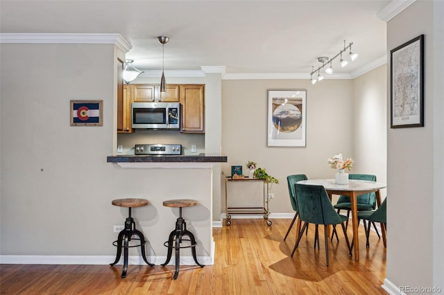 kitchen featuring ornamental molding, appliances with stainless steel finishes, dark countertops, and light wood-style flooring