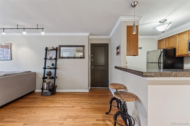 kitchen with light wood finished floors, dark countertops, ornamental molding, brown cabinets, and freestanding refrigerator