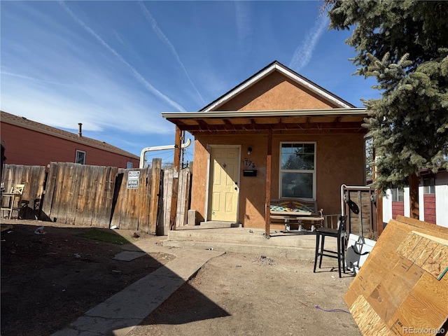 rear view of house featuring stucco siding and fence