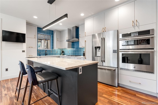 2334 Lowell Blvd, Denver, CO 80211 - kitchen with stainless steel appliances, wall chimney exhaust hood, light wood-style flooring, a breakfast bar area, and light stone countertops