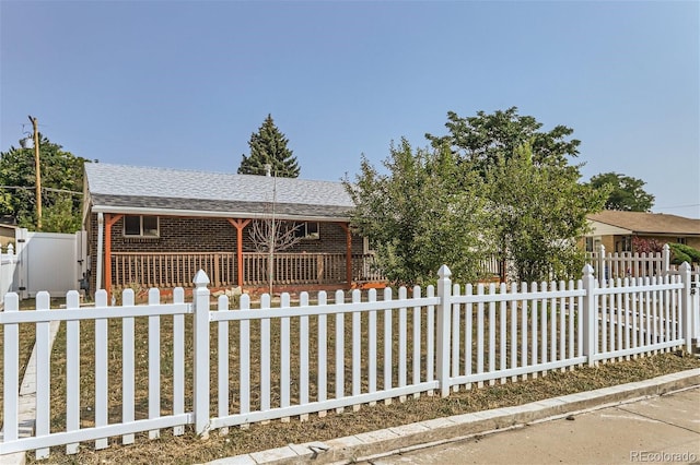 ranch-style home with a fenced front yard, roof with shingles, and brick siding