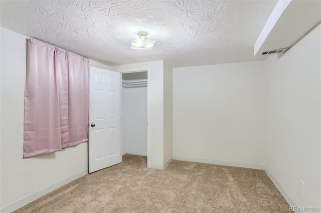 unfurnished bedroom featuring a closet, visible vents, light carpet, a textured ceiling, and baseboards