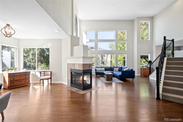 living room featuring a tile fireplace, a healthy amount of sunlight, dark wood-type flooring, and a towering ceiling