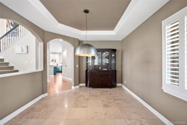 hallway with crown molding, a raised ceiling, light tile patterned floors, and a wealth of natural light