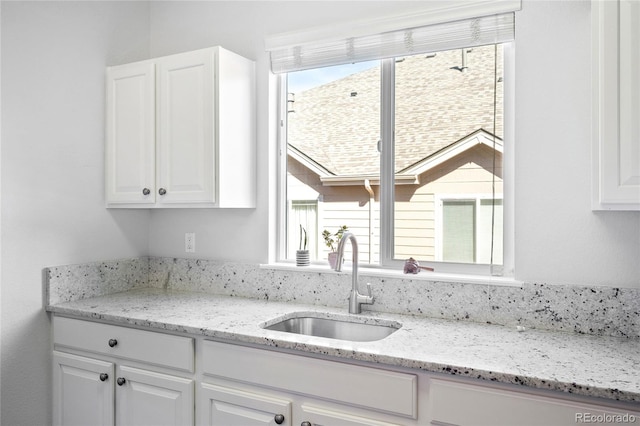 kitchen featuring white cabinetry, sink, and light stone countertops