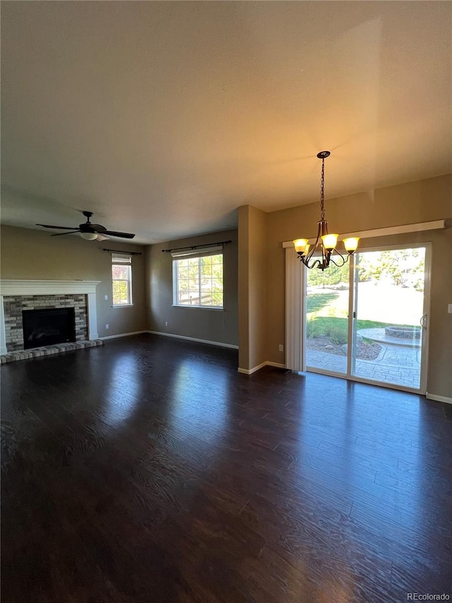 unfurnished living room featuring ceiling fan with notable chandelier, dark wood-type flooring, and a stone fireplace