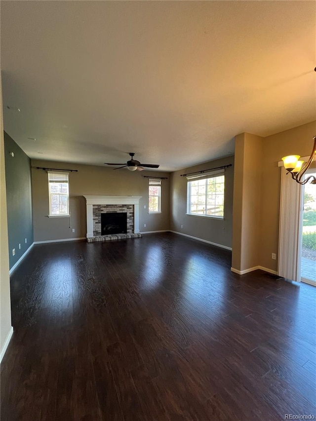 unfurnished living room featuring ceiling fan with notable chandelier, a fireplace, and dark wood-type flooring