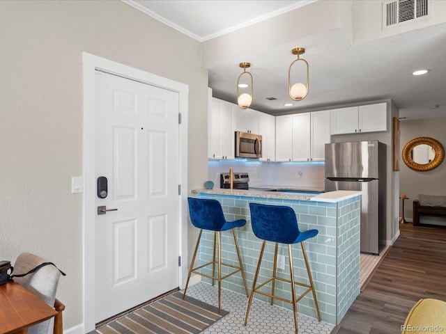 kitchen featuring hanging light fixtures, appliances with stainless steel finishes, kitchen peninsula, decorative backsplash, and white cabinets