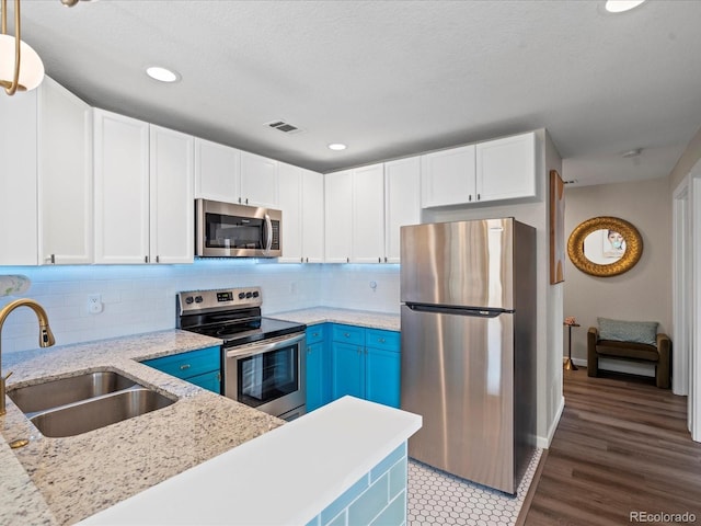 kitchen with appliances with stainless steel finishes, white cabinetry, sink, hanging light fixtures, and light stone countertops