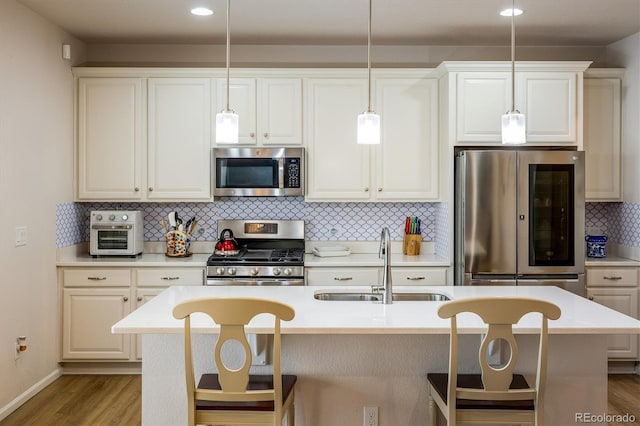 kitchen with an island with sink, appliances with stainless steel finishes, sink, and pendant lighting