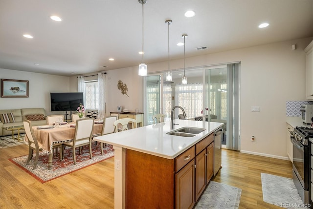 kitchen featuring decorative light fixtures, dishwasher, sink, an island with sink, and range with gas stovetop