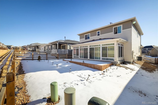 snow covered house featuring central AC and a sunroom