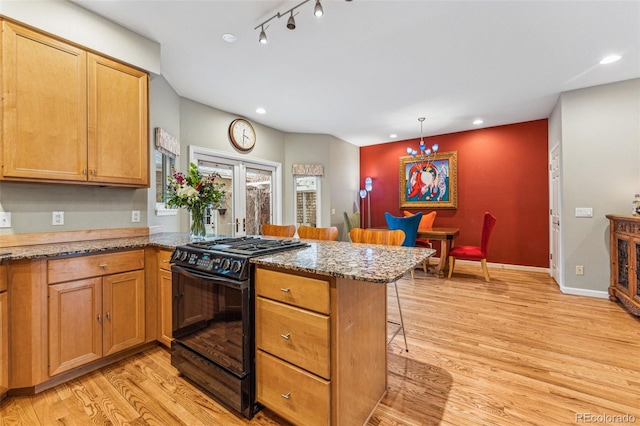 kitchen with black gas range oven, light wood finished floors, a peninsula, and a kitchen breakfast bar