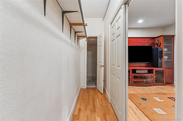 hall featuring baseboards, wood finished floors, and a textured wall