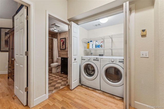 clothes washing area with washing machine and clothes dryer, laundry area, light wood finished floors, and visible vents