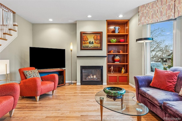 living area featuring wood finished floors, baseboards, recessed lighting, stairs, and a glass covered fireplace