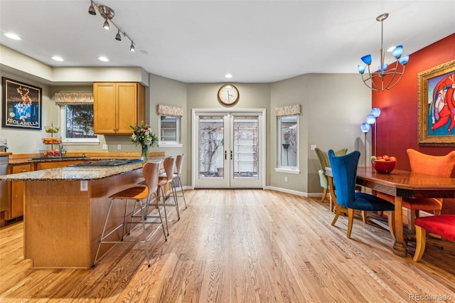 kitchen featuring light stone countertops, baseboards, light wood finished floors, a sink, and french doors