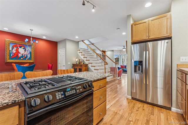 kitchen with light wood-style flooring, recessed lighting, track lighting, black gas range, and stainless steel fridge