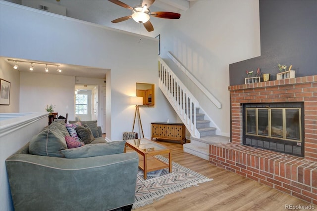 living room featuring stairway, a ceiling fan, a fireplace, wood finished floors, and a towering ceiling