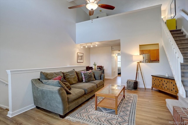 living area with a high ceiling, stairway, light wood finished floors, and ceiling fan