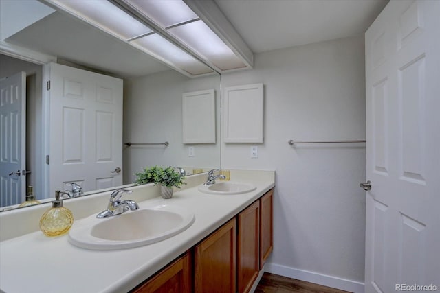 full bath featuring double vanity, wood finished floors, baseboards, and a sink