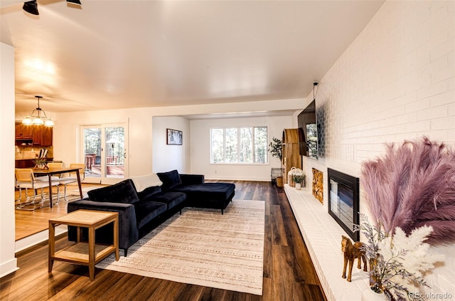 living room featuring a brick fireplace, dark wood-style flooring, baseboards, and brick wall