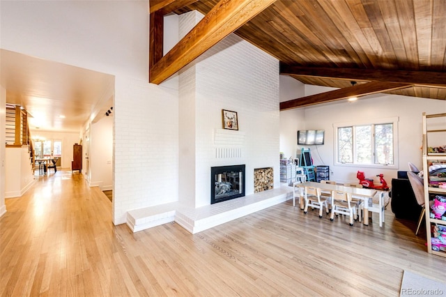 living area with a large fireplace, plenty of natural light, light wood finished floors, and beamed ceiling